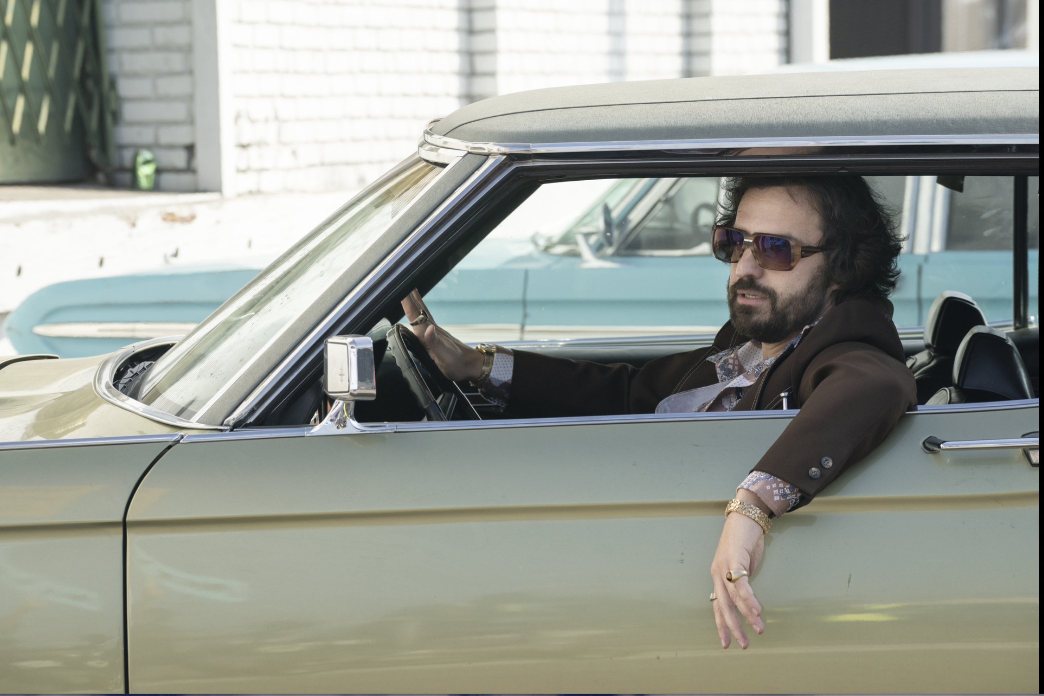 Jake Johnson in a car with one arm out the window.