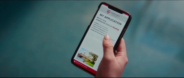 Mandy's hand holding her phone with an image of her online application status showing pending on the screen.